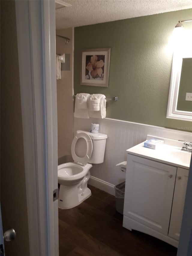 bathroom with a textured ceiling, wood-type flooring, vanity, and toilet