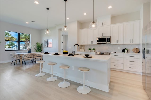 kitchen featuring white cabinetry, a kitchen bar, stainless steel appliances, a center island with sink, and decorative light fixtures