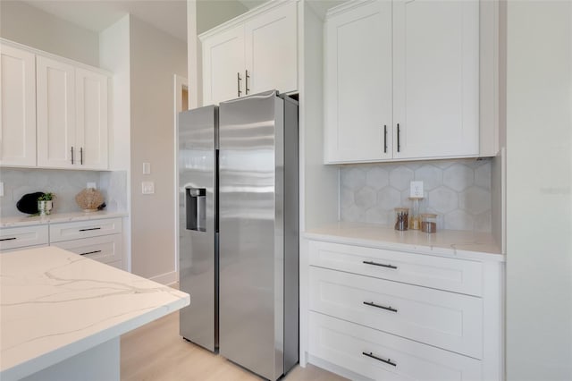 kitchen with light stone counters, light hardwood / wood-style floors, stainless steel refrigerator with ice dispenser, white cabinetry, and decorative backsplash