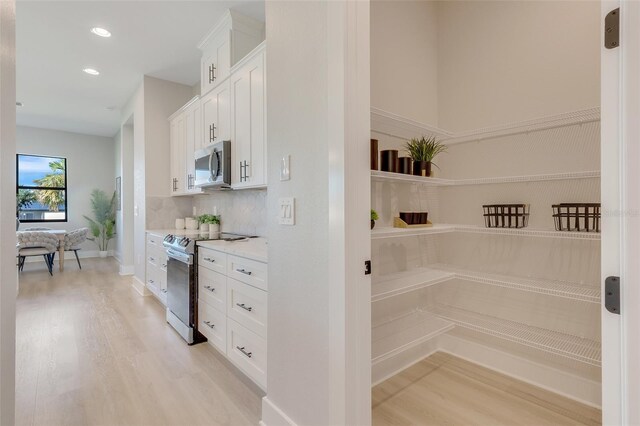 kitchen with light stone counters, light hardwood / wood-style flooring, appliances with stainless steel finishes, and white cabinetry