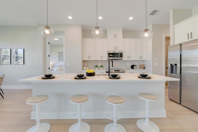 kitchen featuring decorative light fixtures, a center island with sink, and stainless steel appliances