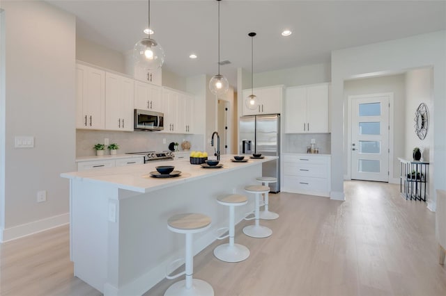 kitchen with a kitchen island with sink, white cabinetry, stainless steel appliances, a kitchen bar, and decorative backsplash