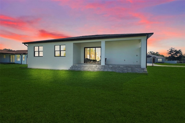 back house at dusk featuring a lawn and a patio