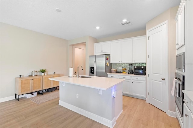 kitchen with light hardwood / wood-style floors, sink, an island with sink, white cabinetry, and stainless steel appliances