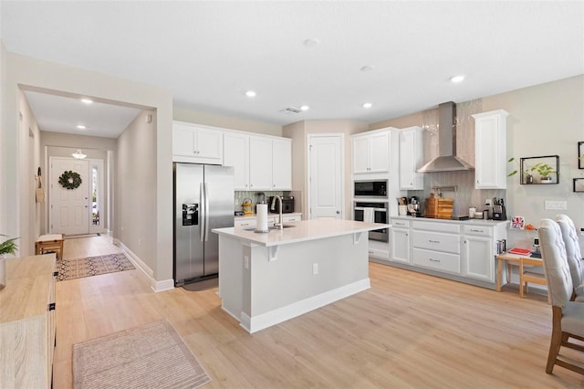 kitchen with a center island with sink, light hardwood / wood-style flooring, stainless steel fridge, and wall chimney range hood