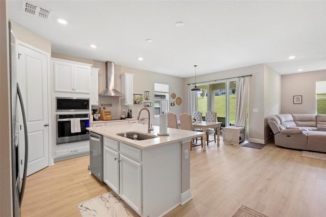 kitchen with white cabinets, an island with sink, wall chimney exhaust hood, and hanging light fixtures