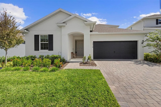 view of front of house with a front lawn, decorative driveway, an attached garage, and stucco siding