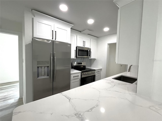 kitchen with white cabinetry, appliances with stainless steel finishes, sink, and light stone countertops