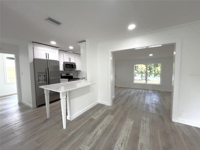 kitchen with light hardwood / wood-style floors, kitchen peninsula, a breakfast bar area, white cabinetry, and appliances with stainless steel finishes