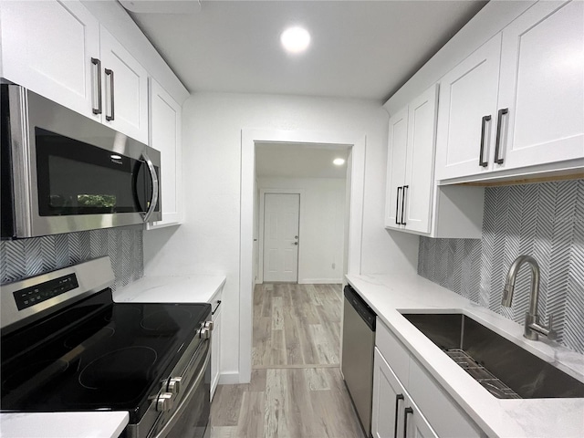 kitchen with sink, appliances with stainless steel finishes, light stone countertops, light hardwood / wood-style flooring, and white cabinets