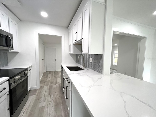 kitchen featuring light stone counters, light wood-type flooring, appliances with stainless steel finishes, sink, and white cabinets