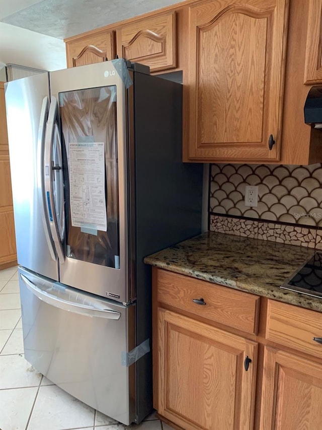 kitchen featuring black stovetop, dark stone counters, stainless steel fridge, and light tile patterned floors