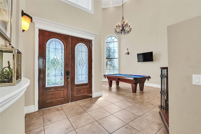 foyer entrance featuring a towering ceiling, billiards, light tile patterned floors, crown molding, and a notable chandelier