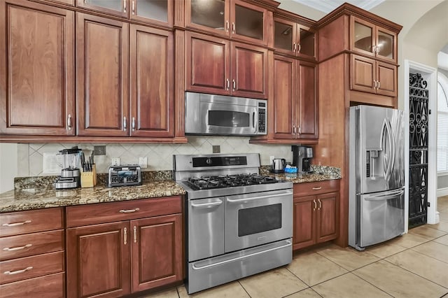 kitchen with stainless steel appliances, backsplash, light tile patterned floors, and dark stone counters