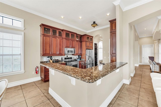 kitchen with light tile patterned flooring, ornamental molding, appliances with stainless steel finishes, a breakfast bar, and dark stone counters