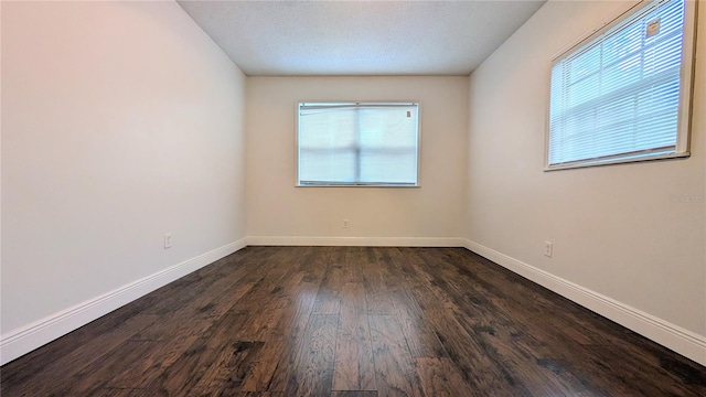 spare room featuring a textured ceiling, a healthy amount of sunlight, and dark hardwood / wood-style flooring