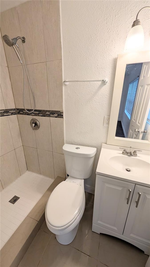 bathroom with vanity, toilet, a tile shower, and tile patterned floors