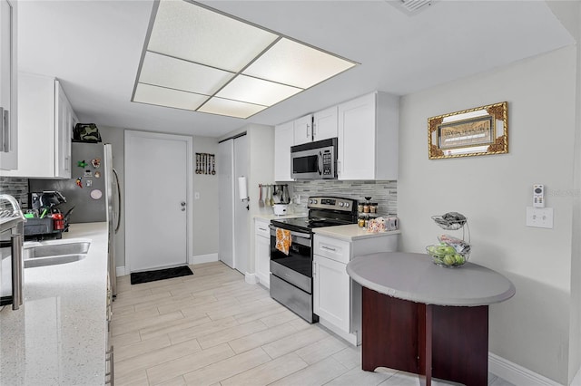 kitchen with white cabinetry, backsplash, stainless steel appliances, and light stone counters