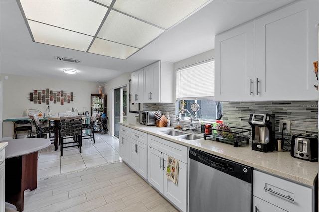 kitchen featuring white cabinets, backsplash, light stone countertops, stainless steel dishwasher, and sink