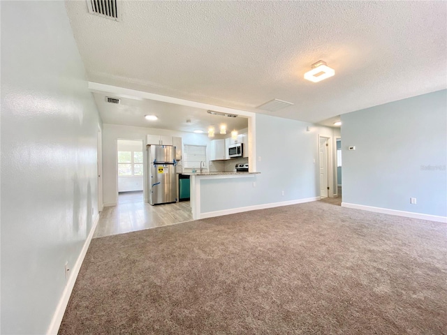 unfurnished living room featuring light carpet and a textured ceiling