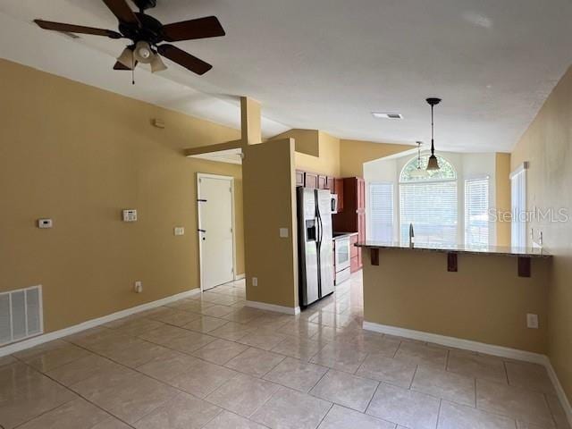 kitchen with a breakfast bar, lofted ceiling, decorative light fixtures, ceiling fan, and stainless steel fridge