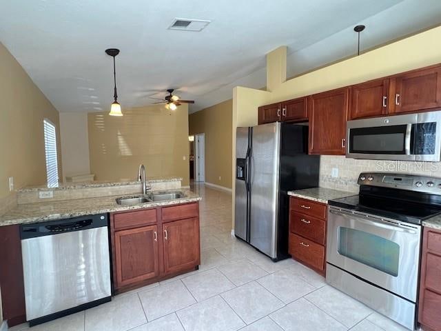 kitchen featuring light stone counters, pendant lighting, light tile patterned floors, sink, and appliances with stainless steel finishes