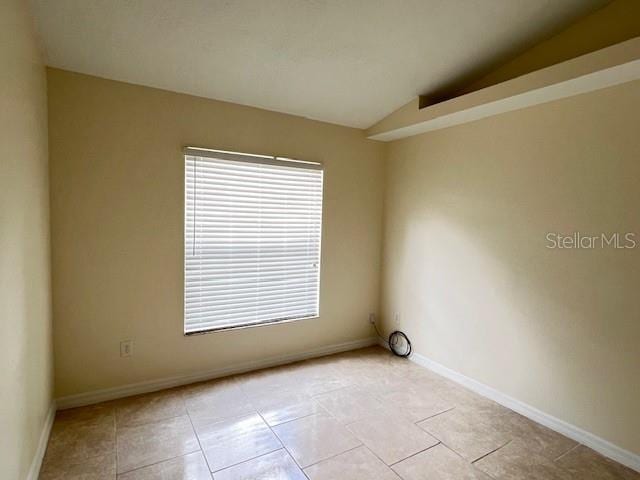 tiled spare room featuring lofted ceiling