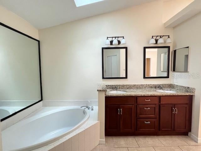 bathroom with vanity, tiled bath, lofted ceiling with skylight, and tile patterned floors