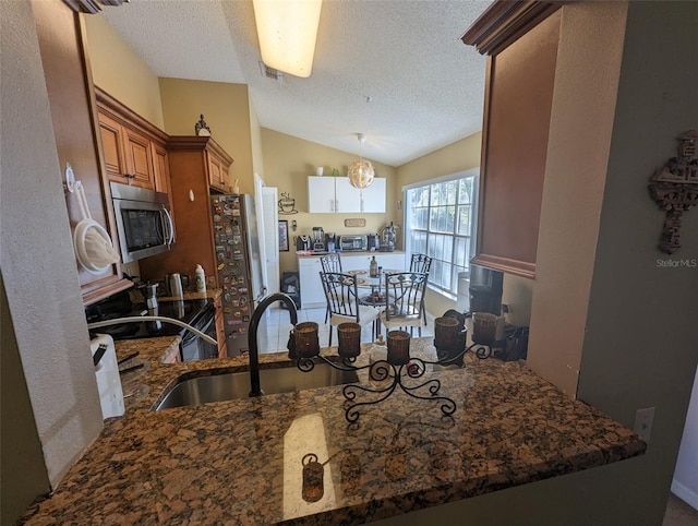 kitchen with kitchen peninsula, appliances with stainless steel finishes, a textured ceiling, vaulted ceiling, and sink