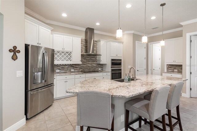 kitchen with stainless steel appliances, hanging light fixtures, an island with sink, and wall chimney exhaust hood