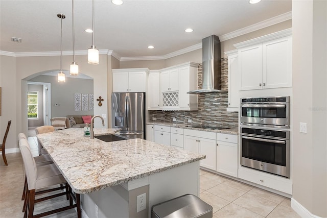 kitchen with a large island with sink, stainless steel appliances, white cabinets, wall chimney exhaust hood, and sink