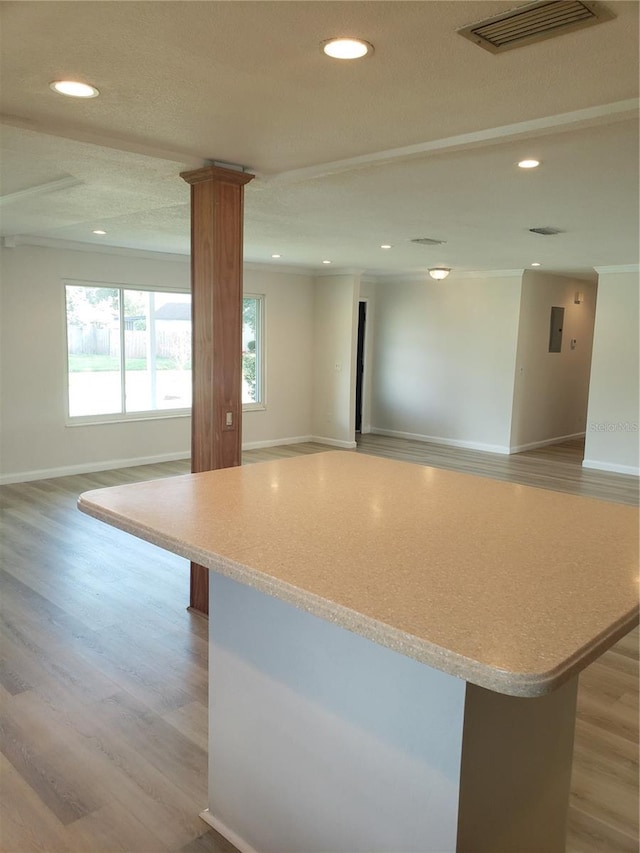 kitchen featuring ornamental molding, light hardwood / wood-style floors, decorative columns, and a kitchen island