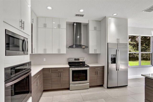 kitchen featuring white cabinets, a textured ceiling, appliances with stainless steel finishes, and wall chimney exhaust hood