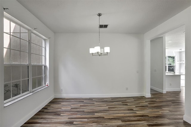 unfurnished dining area featuring dark hardwood / wood-style floors, an inviting chandelier, and a textured ceiling