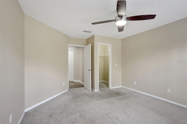 unfurnished bedroom featuring a spacious closet, ceiling fan, a closet, light colored carpet, and a textured ceiling