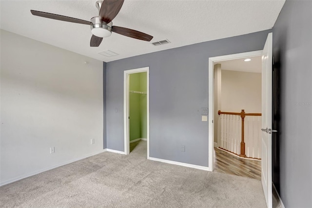 unfurnished bedroom with ceiling fan, a closet, light carpet, a walk in closet, and a textured ceiling