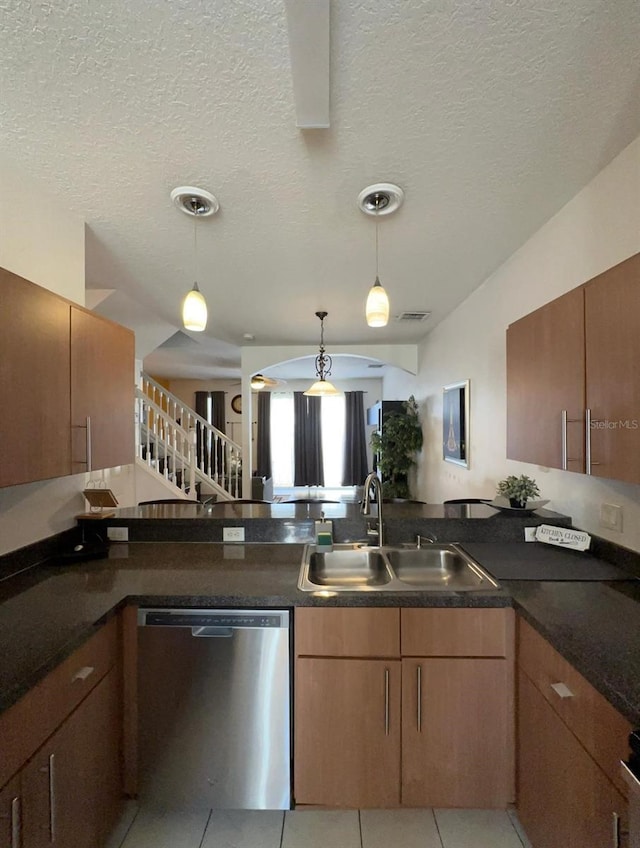 kitchen with a textured ceiling, stainless steel dishwasher, sink, and pendant lighting