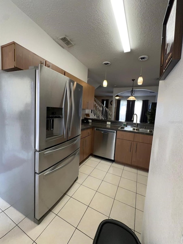 kitchen with pendant lighting, a textured ceiling, light tile patterned flooring, sink, and stainless steel appliances