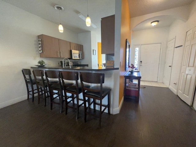 kitchen with a kitchen breakfast bar, dark wood-type flooring, kitchen peninsula, pendant lighting, and sink