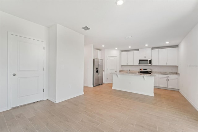 kitchen featuring white cabinets, appliances with stainless steel finishes, an island with sink, and light hardwood / wood-style flooring