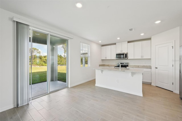 kitchen featuring a breakfast bar, a center island with sink, light stone countertops, white cabinetry, and stainless steel appliances