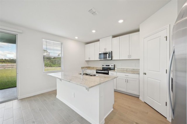 kitchen featuring appliances with stainless steel finishes, light stone counters, a center island with sink, white cabinets, and a breakfast bar area