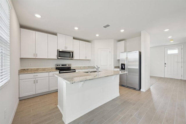 kitchen with a kitchen island with sink, sink, light stone countertops, white cabinetry, and stainless steel appliances