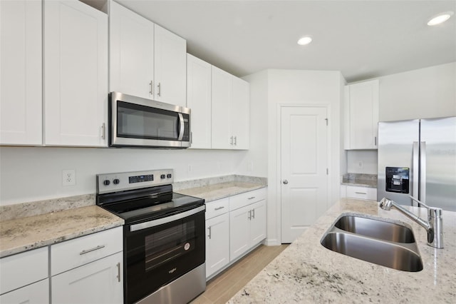 kitchen with light stone countertops, appliances with stainless steel finishes, sink, white cabinets, and light hardwood / wood-style floors