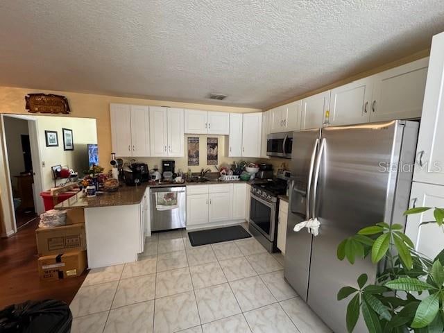 kitchen with kitchen peninsula, appliances with stainless steel finishes, a textured ceiling, and white cabinetry