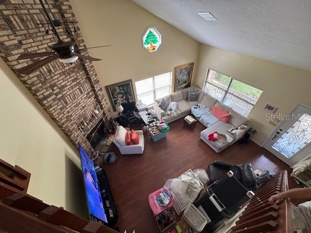 living room with a textured ceiling, ceiling fan, hardwood / wood-style flooring, high vaulted ceiling, and a fireplace