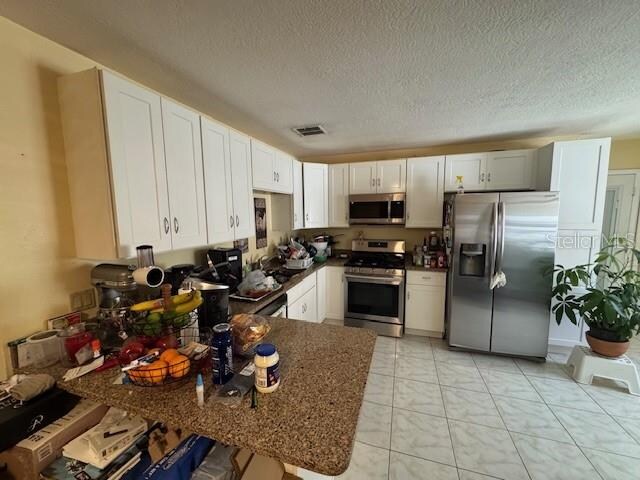 kitchen with white cabinets, dark stone countertops, stainless steel appliances, and a textured ceiling