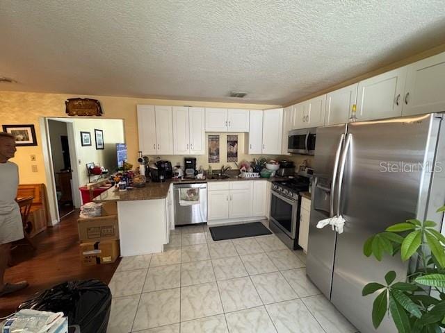 kitchen with white cabinets, a textured ceiling, stainless steel appliances, and kitchen peninsula