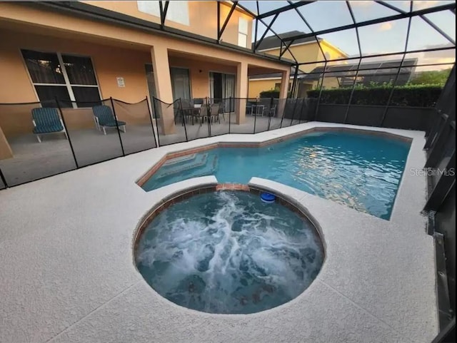 pool at dusk with a lanai, an in ground hot tub, and a patio