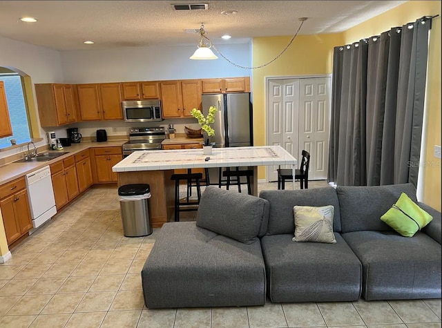 kitchen featuring sink, a textured ceiling, tile counters, a kitchen island, and stainless steel appliances